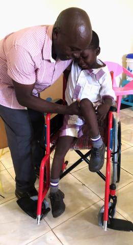 Pius is helped into his new wheelchair by his father 